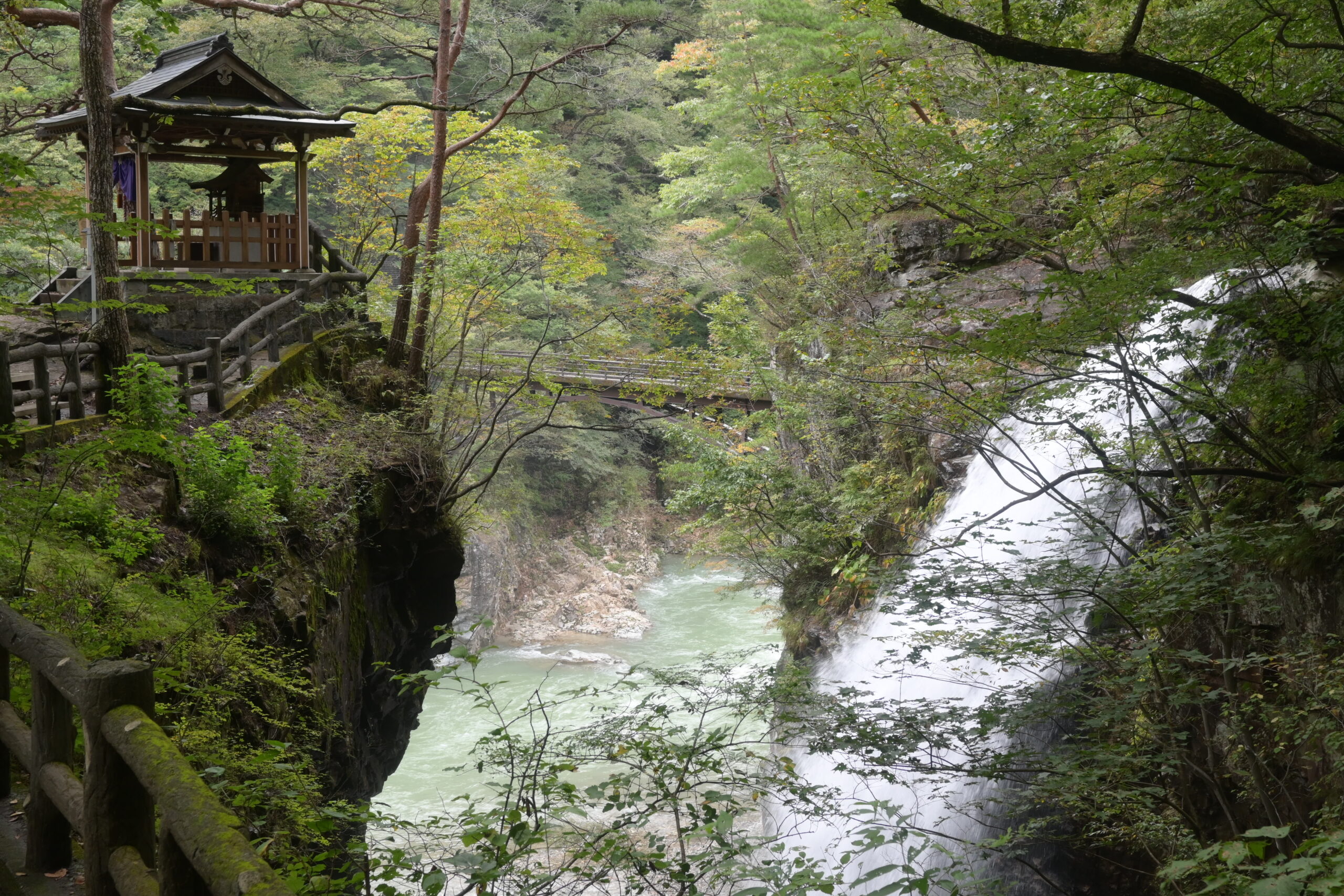 岩肌を流れ落ちる虹見の滝と、その先に見える鬼怒川と虹見橋